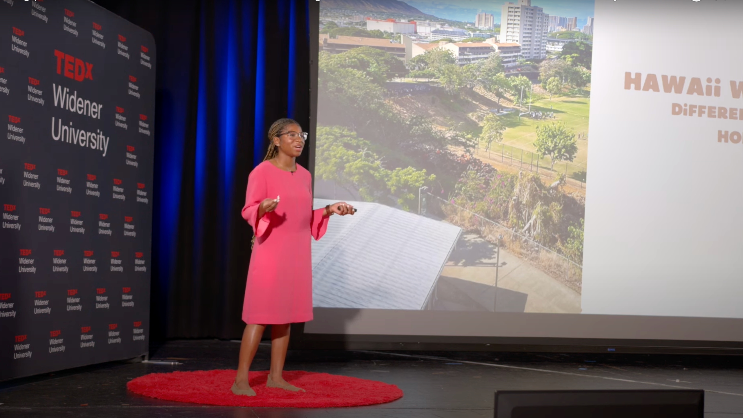 Kendall Gordon TEDxWidenerUniversity 2024 710x400 Widener student on a dark stage in front of a bright background presenting to an unseen audience. Slide depicts her experience studying abroad in Hawaii