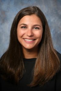 Headshot of professor Emily Battaglia on a blue-grey textured background