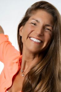 TEDx SPeaker Melissa MRoz with a lrge smile wearing an orange shirt on a white background