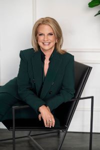 Tracy Davidson in a black suit sitting in a chair in a modern professional environment.